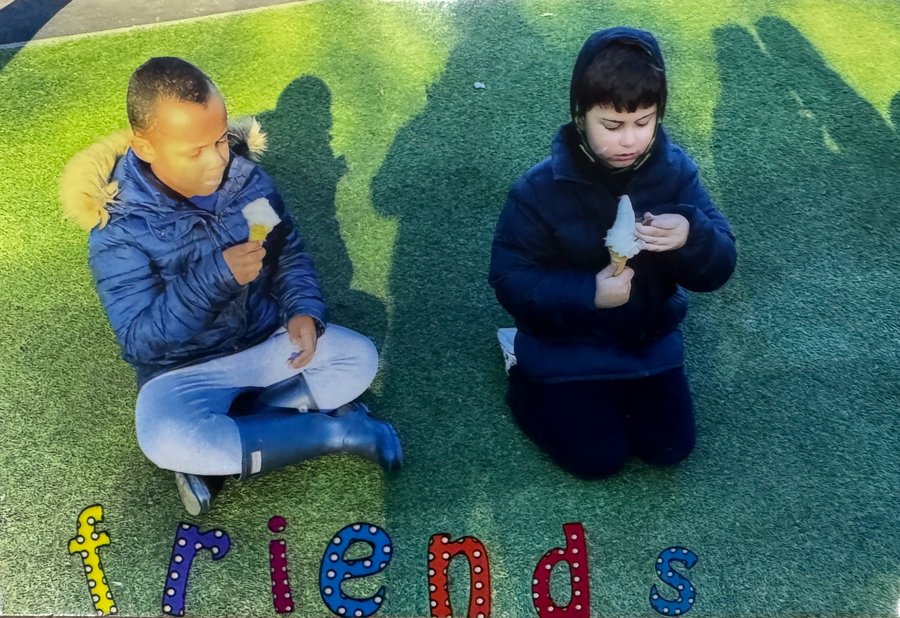 Lucca and Roman eating ice cream on the grass, with the word friends