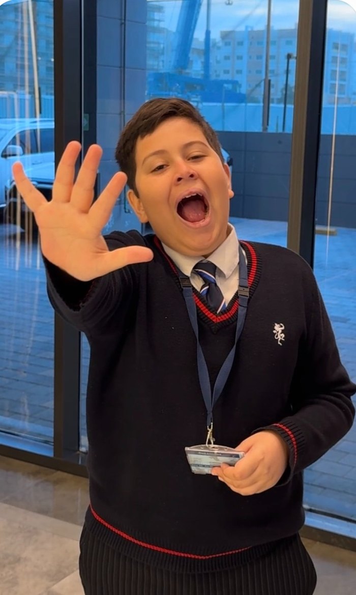 Lucca in his school jumper, smiling and blowing a kiss with his hand outstretched