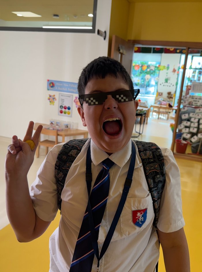 Lucca laughing in his school uniform, wearing pixel sunglasses and making a peace sign